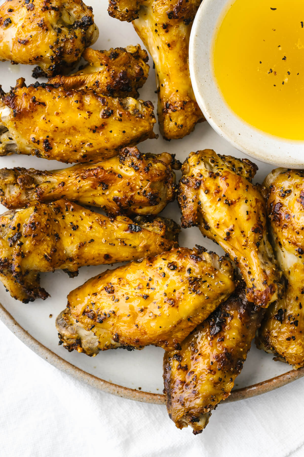 A plate of lemon pepper air fryer chicken wings next to a bowl of sauce.