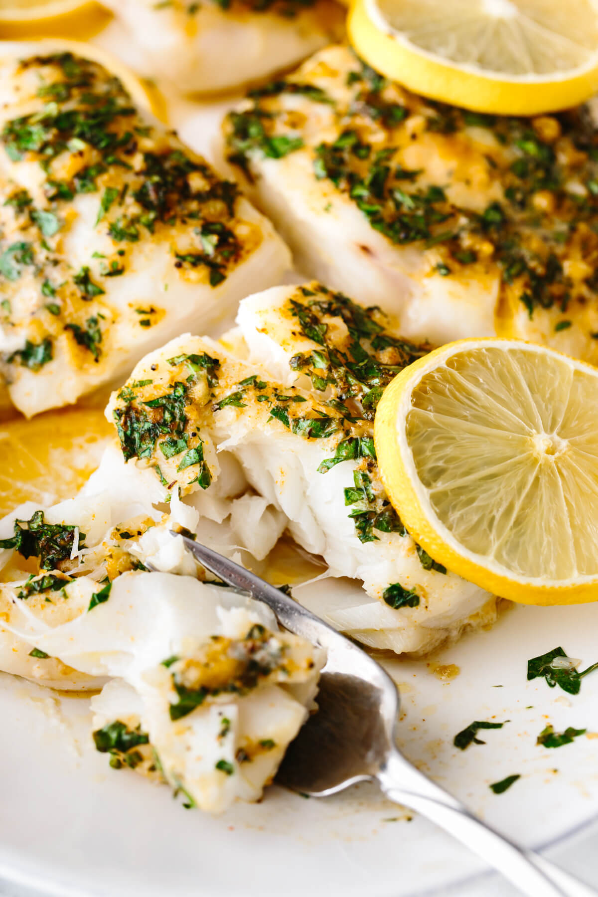 Baked cod being flaked with a fork.