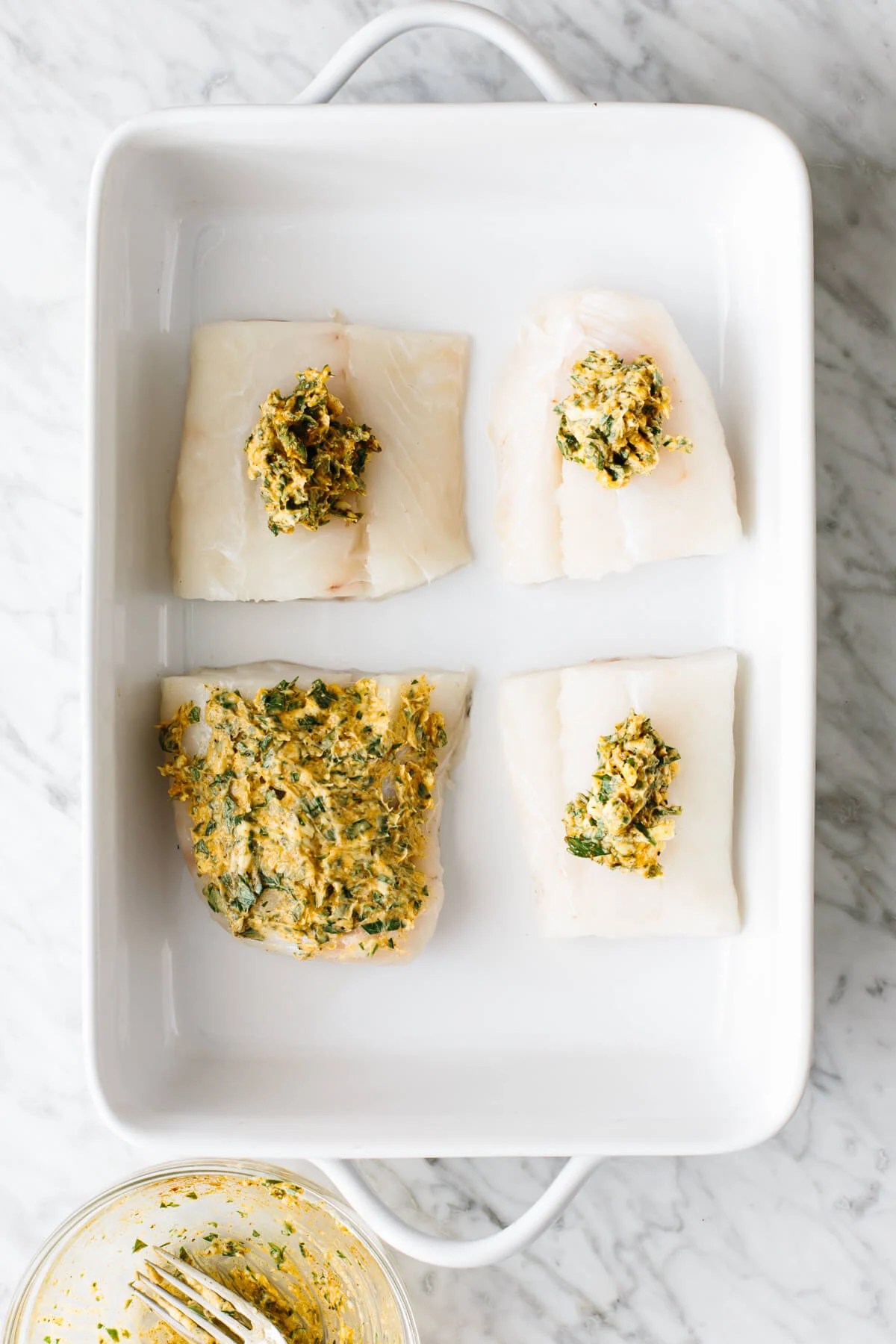Topping cod fillets with garlic herb butter mixture.