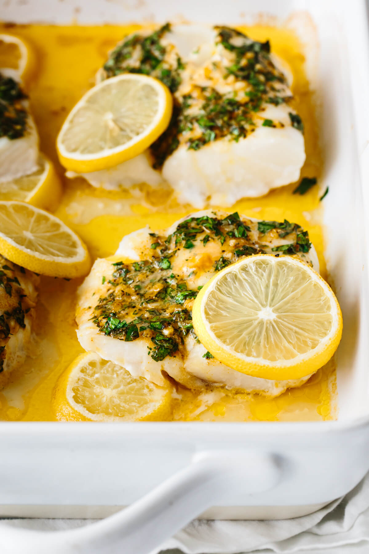 Piece of baked cod with lemon slice in a baking dish.