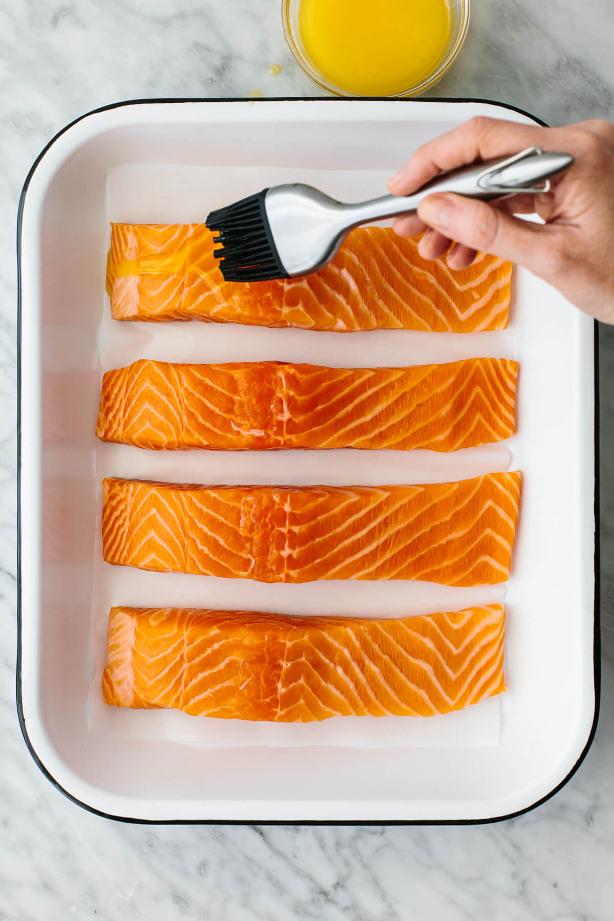 Brushing butter on baked salmon in a pan.