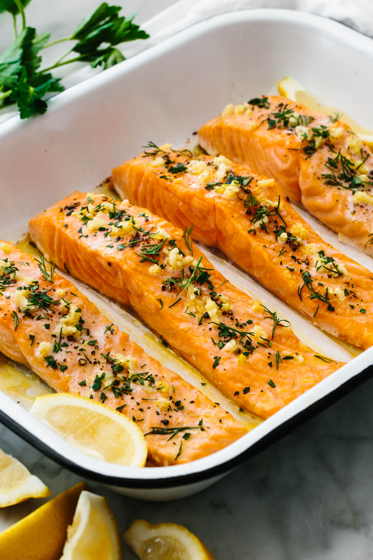 Baked salmon in a pan next to lemon wedges.