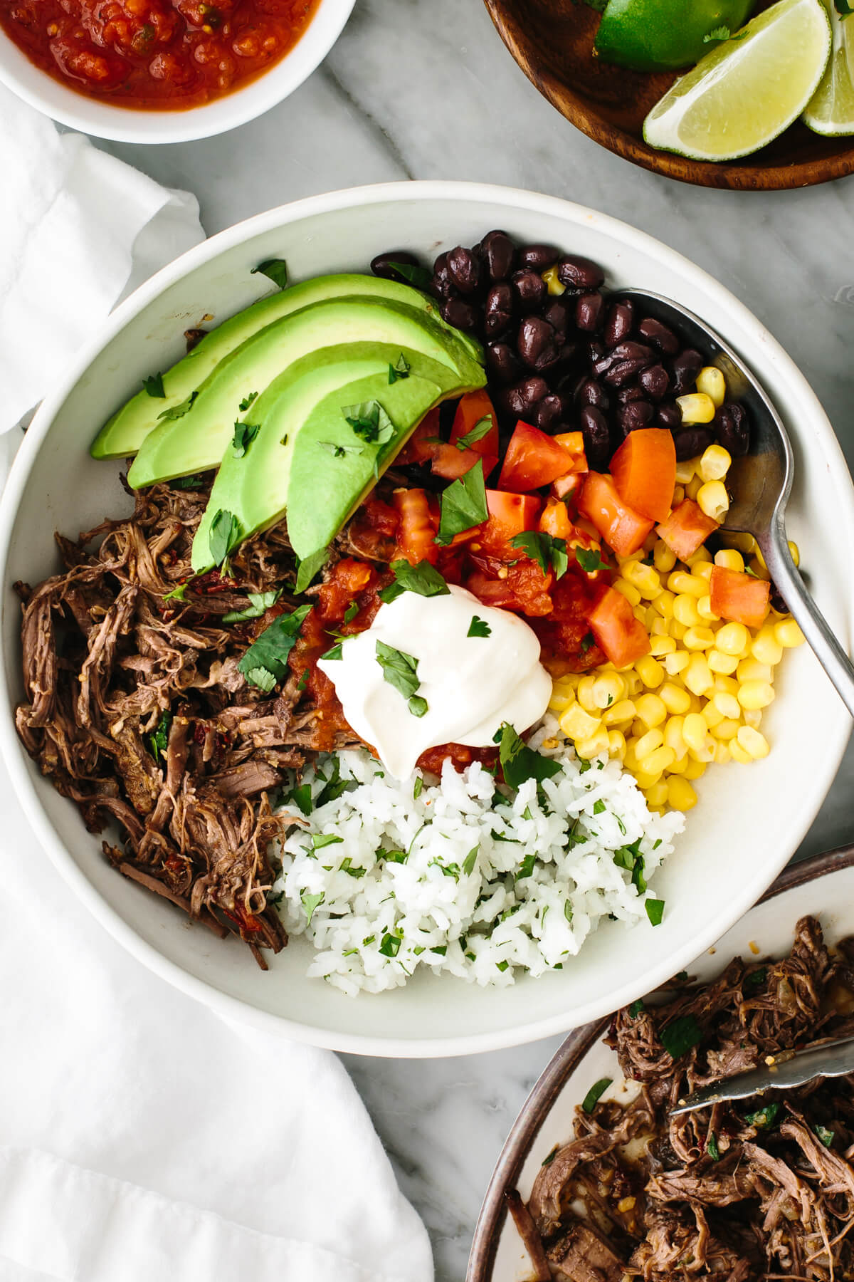 Beef barbacoa burrito bowl on a table with salsa.