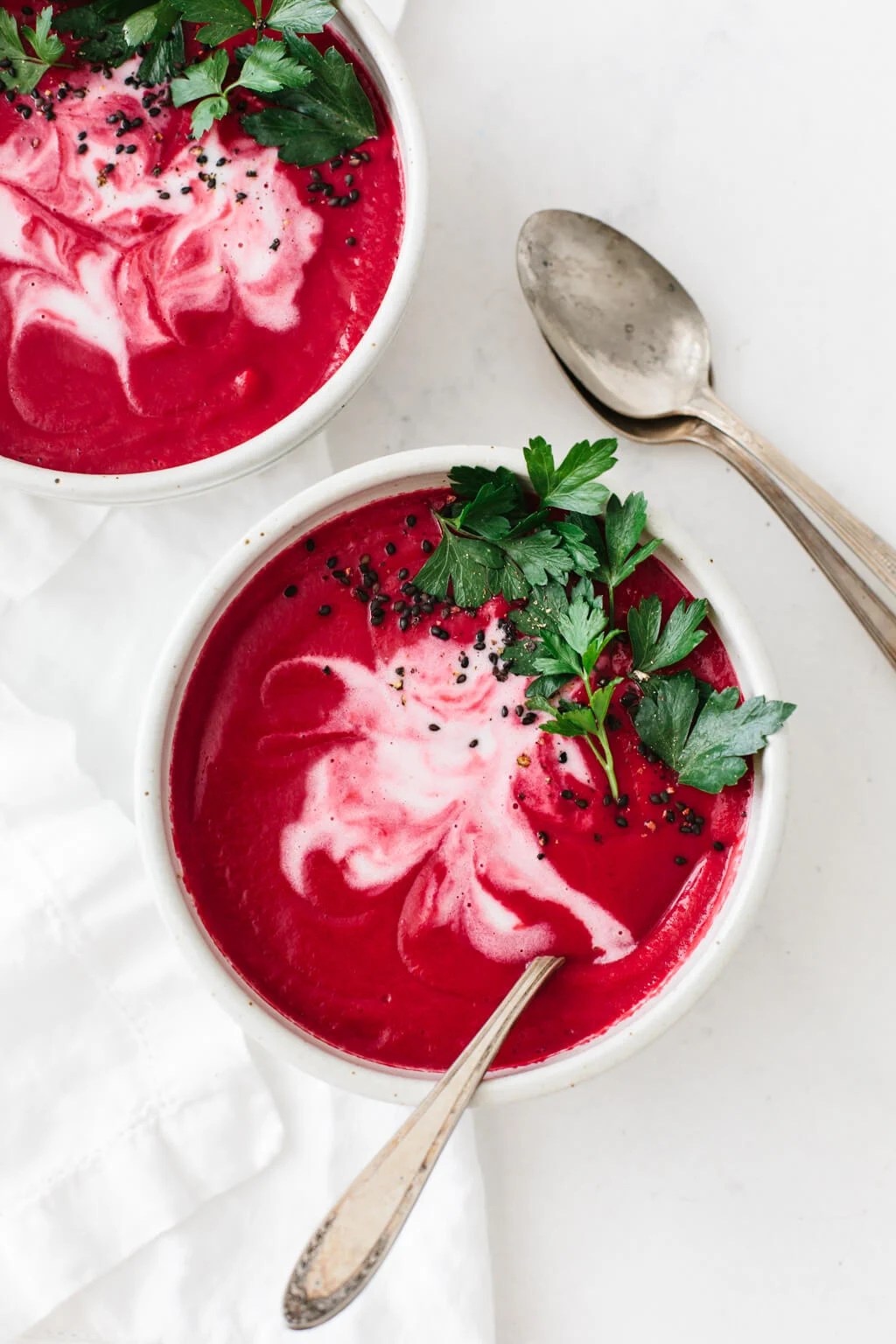 Two bowls of beet soup on a white table.