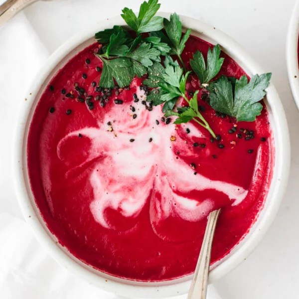 Beet soup in a bowl garnished with coconut cream and parsley.