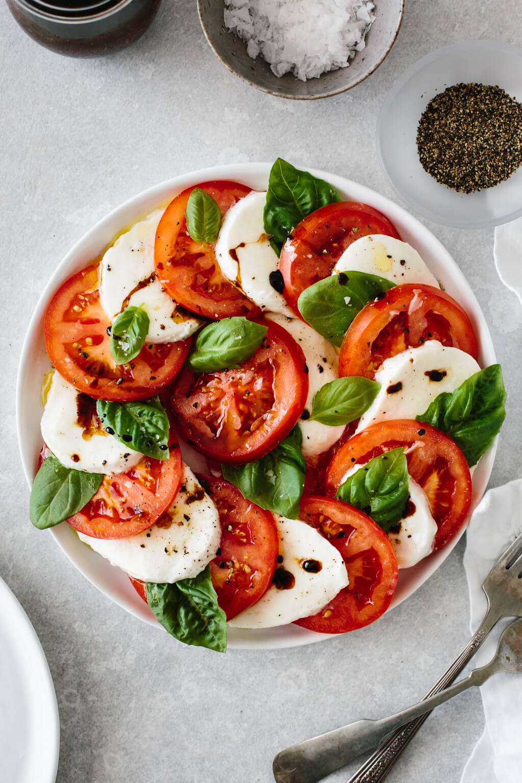 Slices of tomato and mozzarella on a plate with fresh basil leaves.