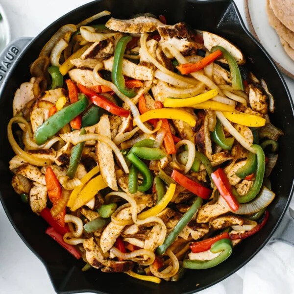 Chicken fajitas in a pan on a table with toppings.