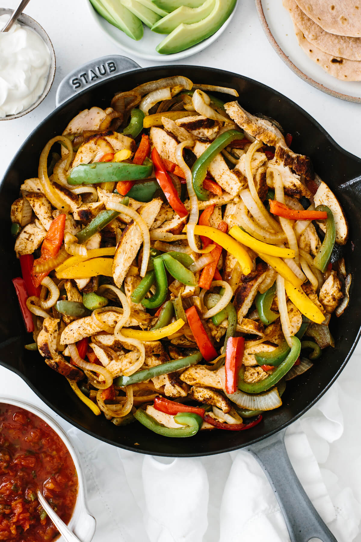 Chicken fajitas in a pan on a table with toppings.
