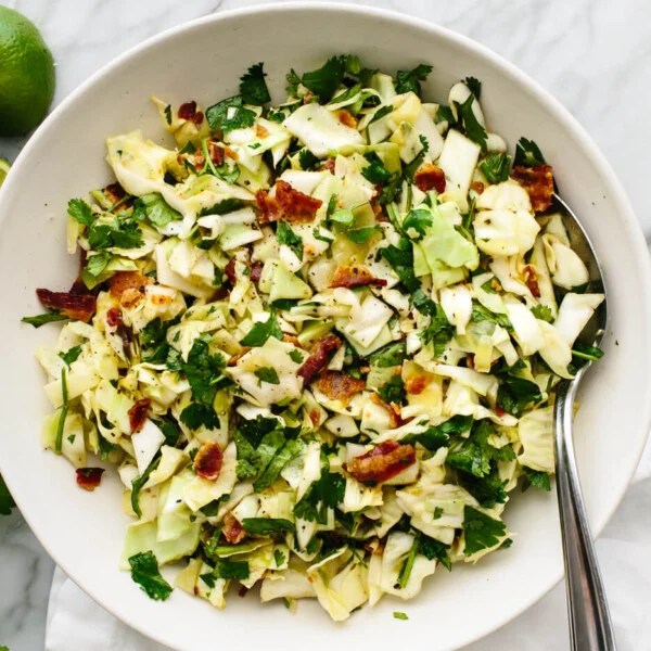 A bowl of cilantro lime bacon coleslaw next to limes.