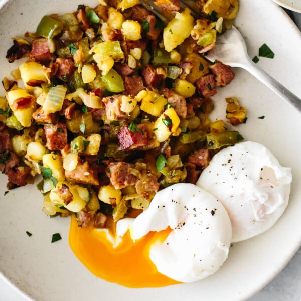 A white plate of corned beef hash and poached eggs