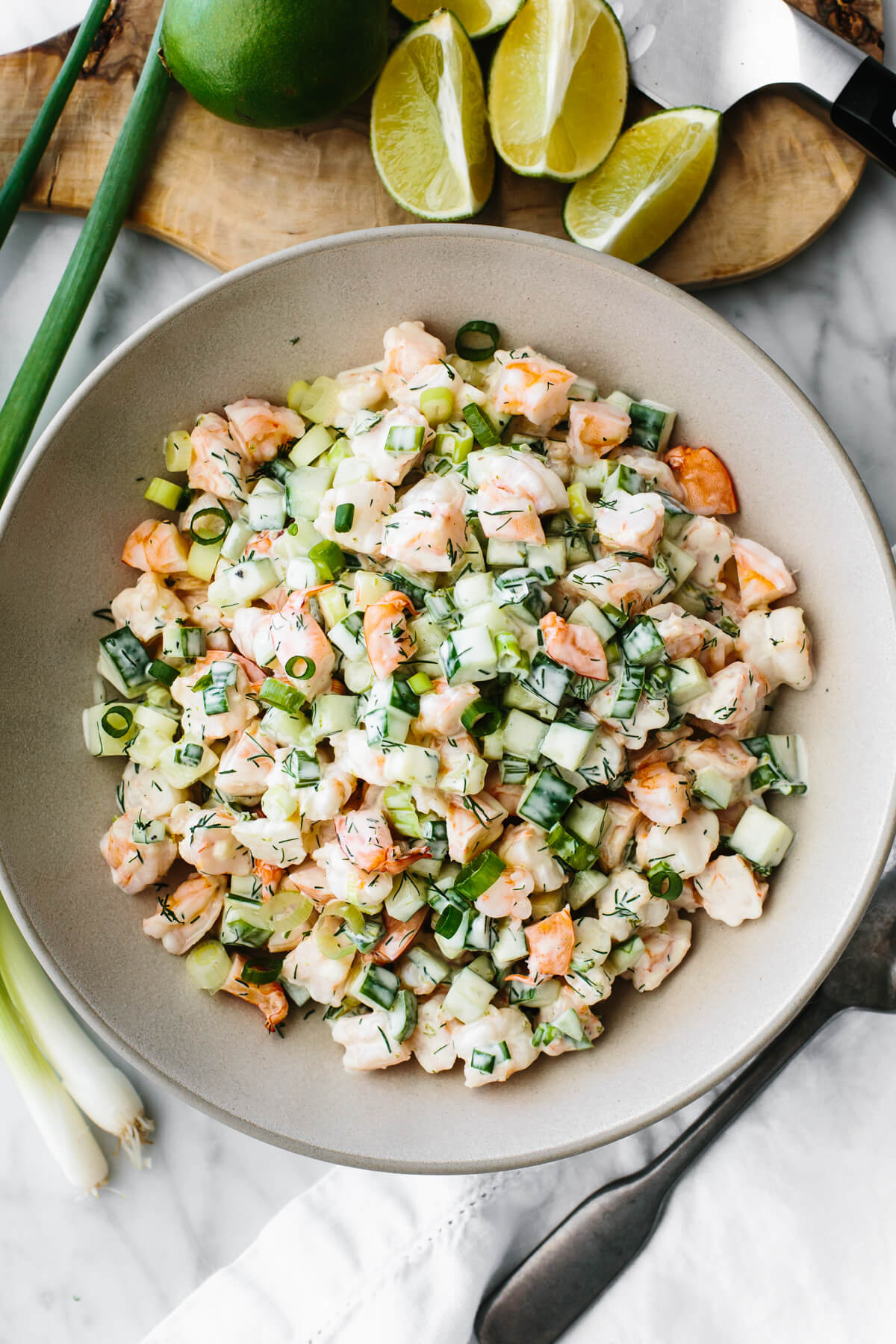 Cucumber shrimp salad in a large serving bowl next to limes