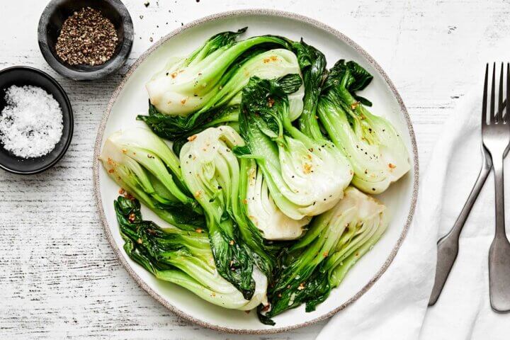 A white plate of cooked baby bok choy.
