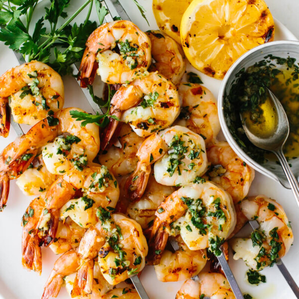 Garlic grilled shrimp skewers on a plate with lemon and parsley.