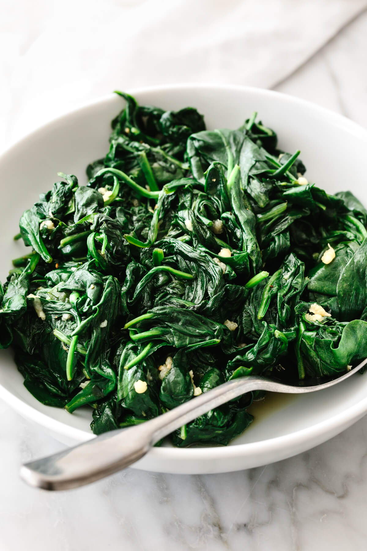 A white bowl with garlic sauteed spinach with a spoon.