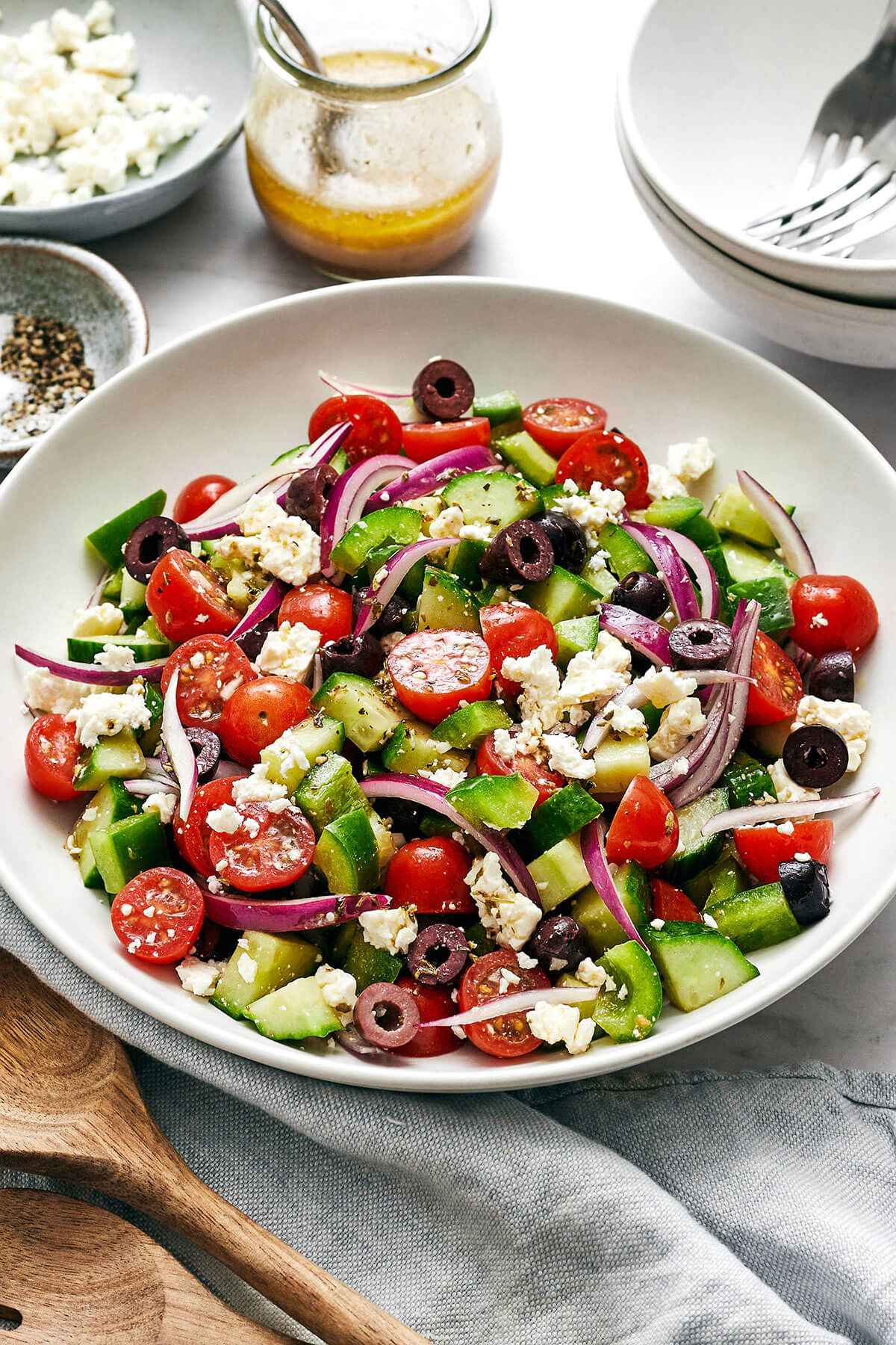Greek salad in a white bowl next to dressing.