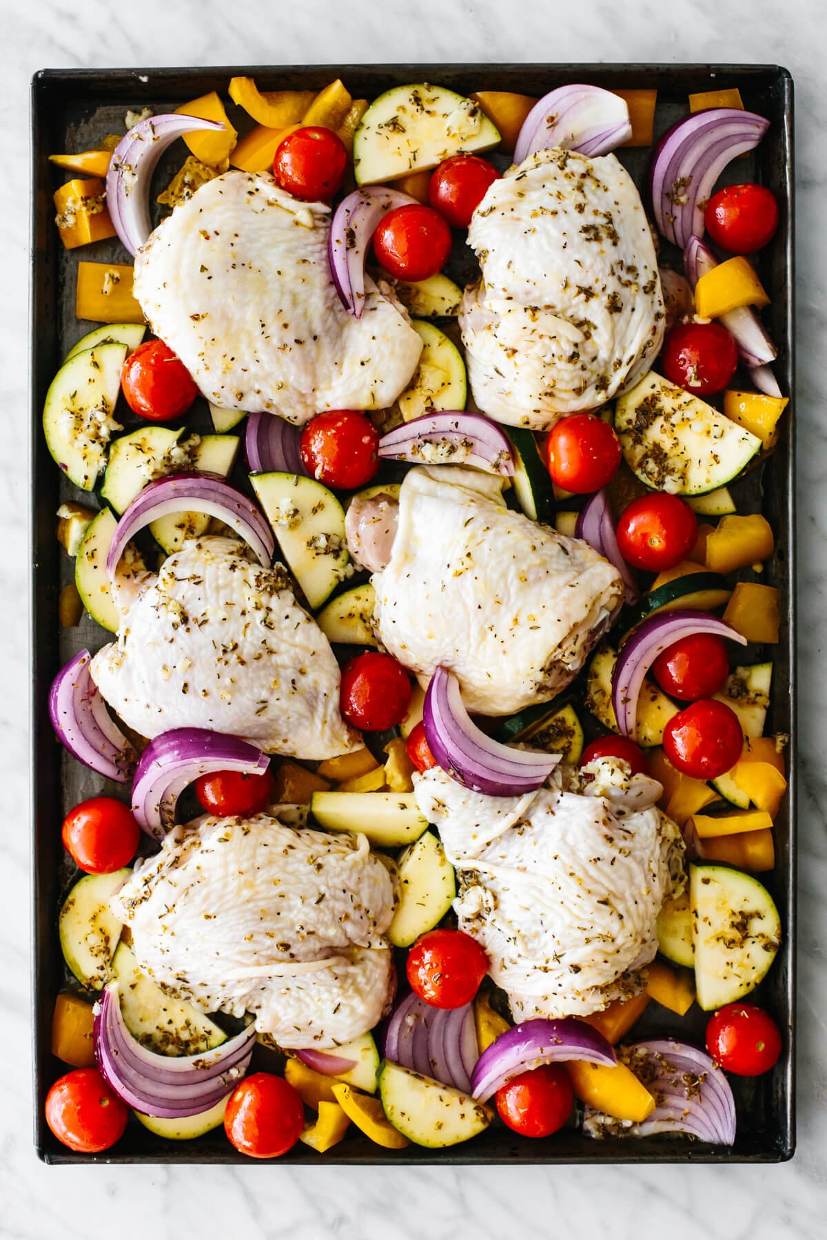 Raw chicken and vegetables on a sheet pan.