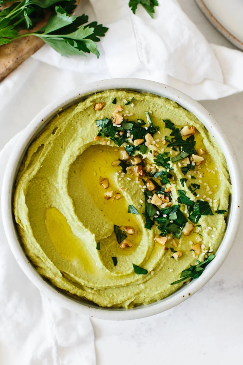 Green hummus in a bowl with herbs and toppings.