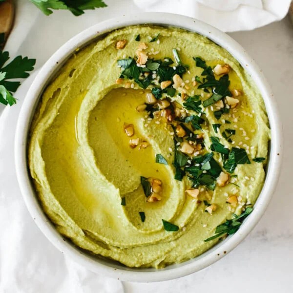 Green hummus in a bowl with herb toppings.