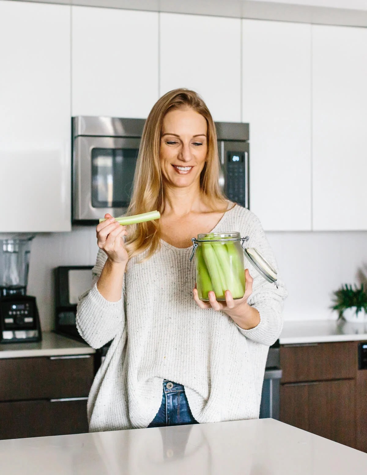 Girl standing in kitchen eating celery sticks.