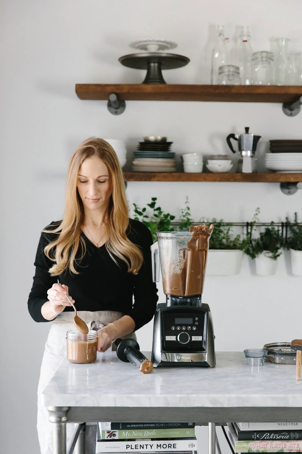 Girl standing next to Vitamix blender with almond butter in it. 