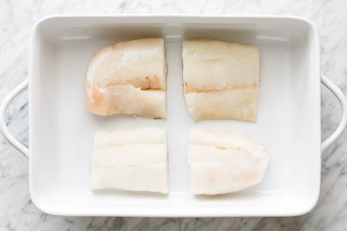 Four cod fillets in a baking dish.