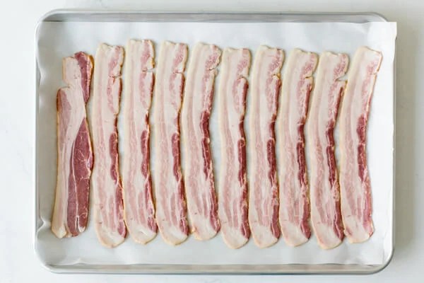 Raw bacon on a parchment lined baking tray.