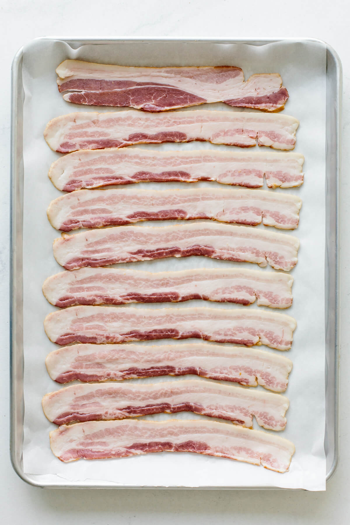 Raw bacon on a sheet tray.