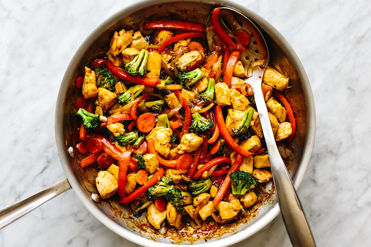 A pan with chicken stir-fry and a slotted spoon.