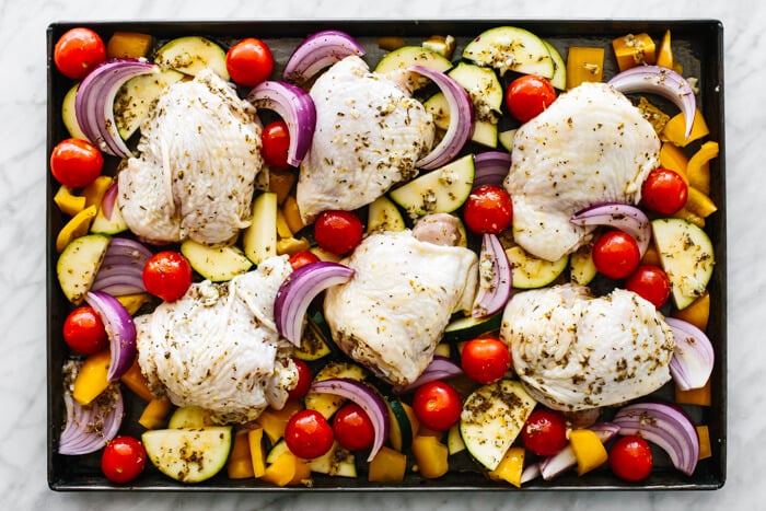 Raw chicken and vegetables on a sheet pan.