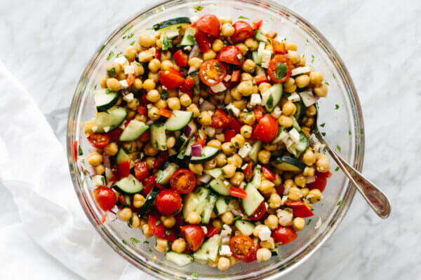 Mediterranean chickpea salad ingredients tossed together in a glass bowl on a table.