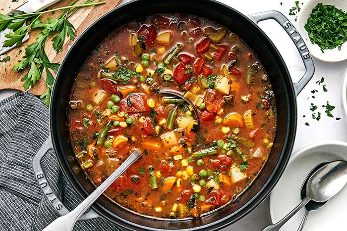 A pot of vegetable soup with a ladel