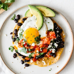 Huevos rancheros on a white plate next to cilantro and cotija cheese.