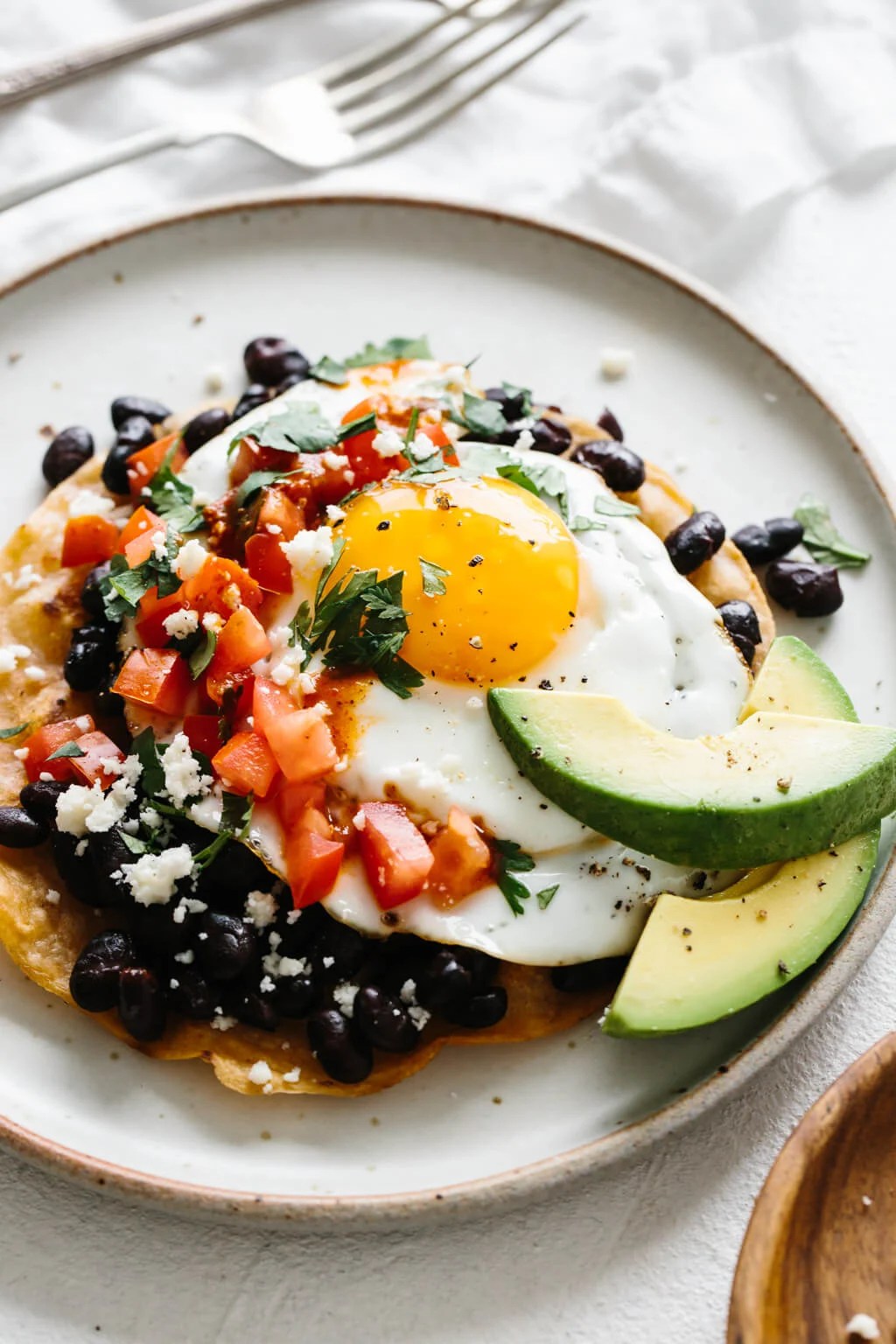 Huevos rancheros on a white plate next to forks.