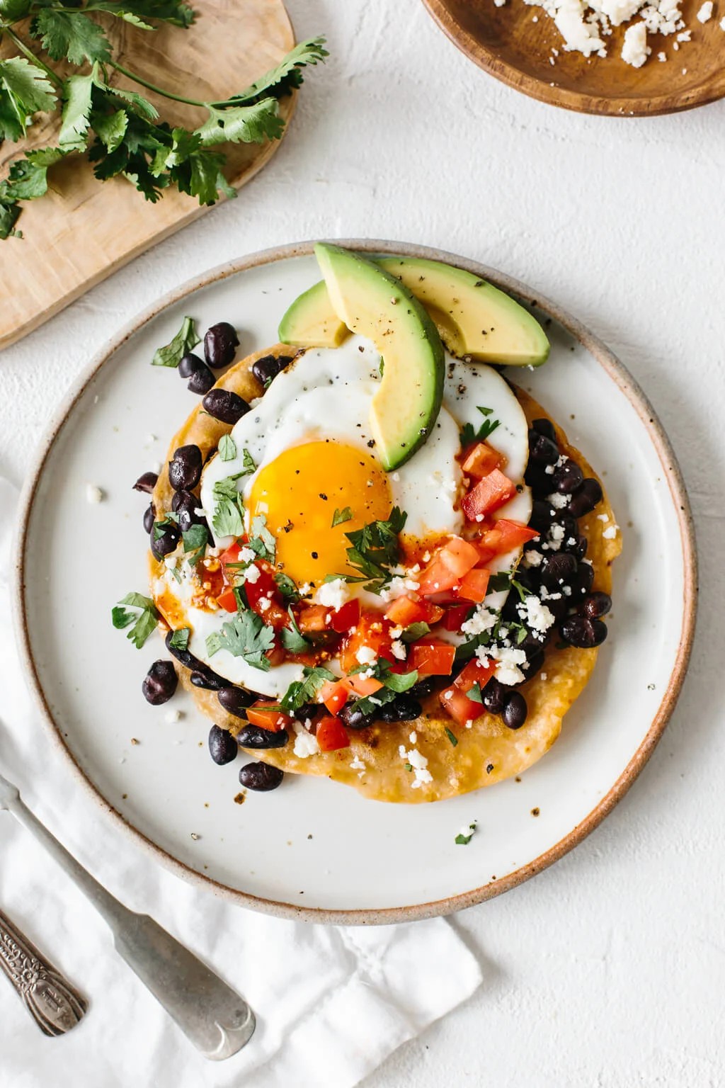 Huevos rancheros on a white plate topped with slices of avocado.