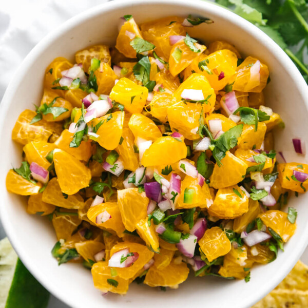 A bowl of mandarin orange salsa next to limes.