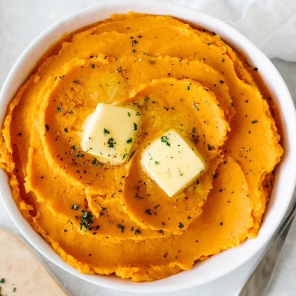 Mashed sweet potatoes in a white bowl topped with butter.