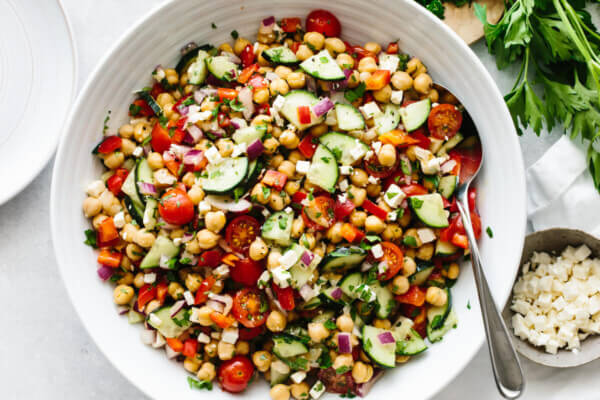 A large white bowl of Mediterranean chickpea salad on a table with parsley leaves.