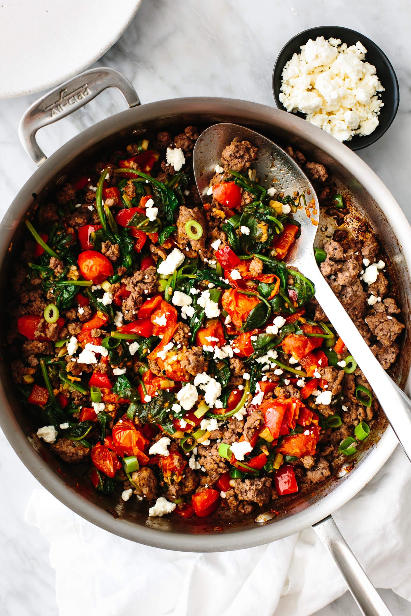 Mediterranean ground beef stir fry in a pan with a slotted spoon.