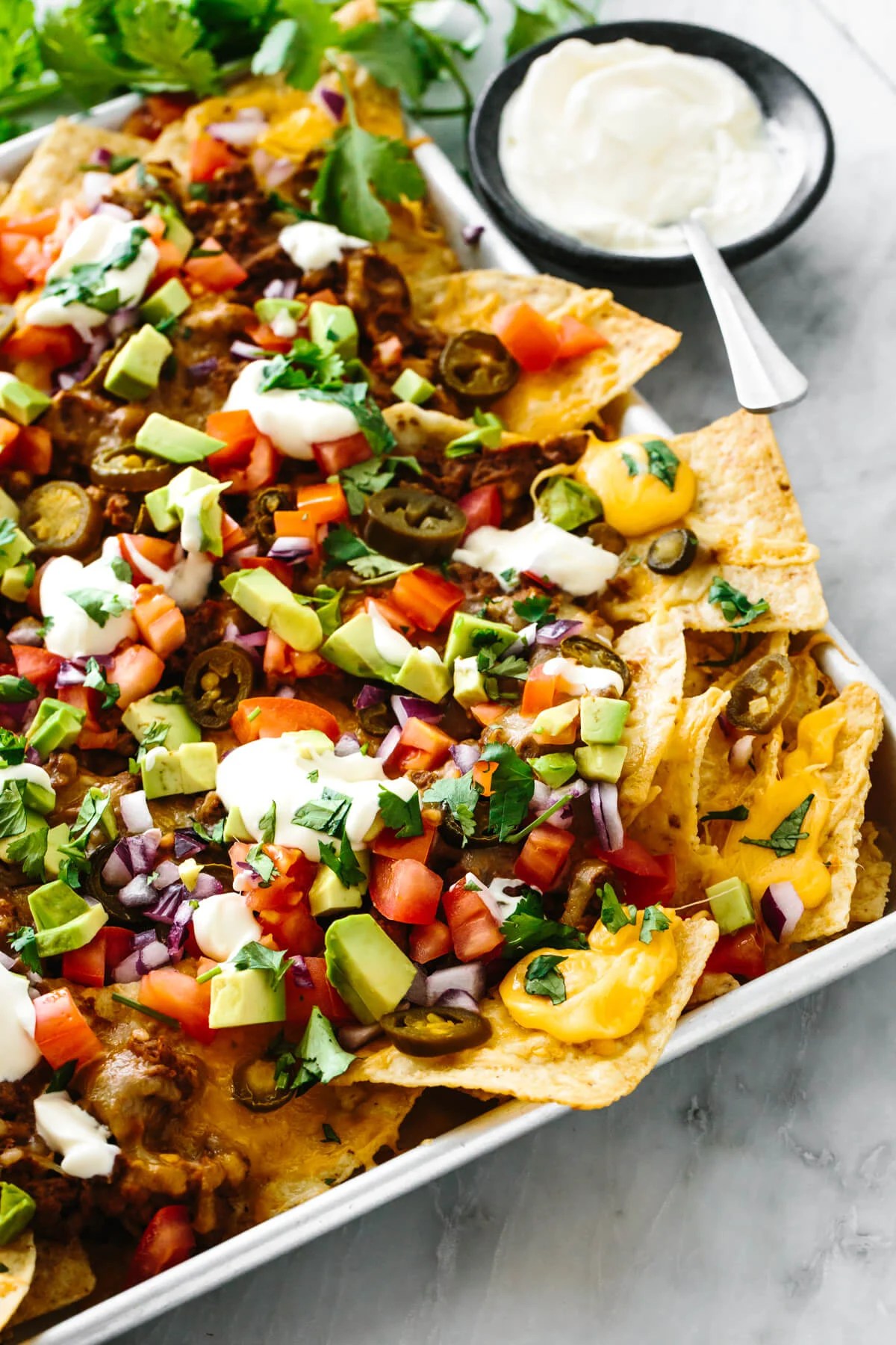 A sheet pan with nachos next to cilantro