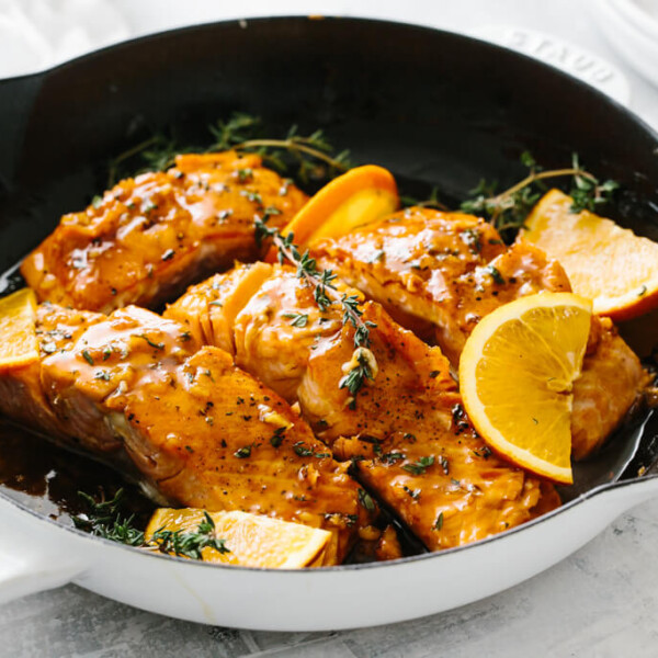 Four salmon filets in a pan with orange slices and thyme on top.