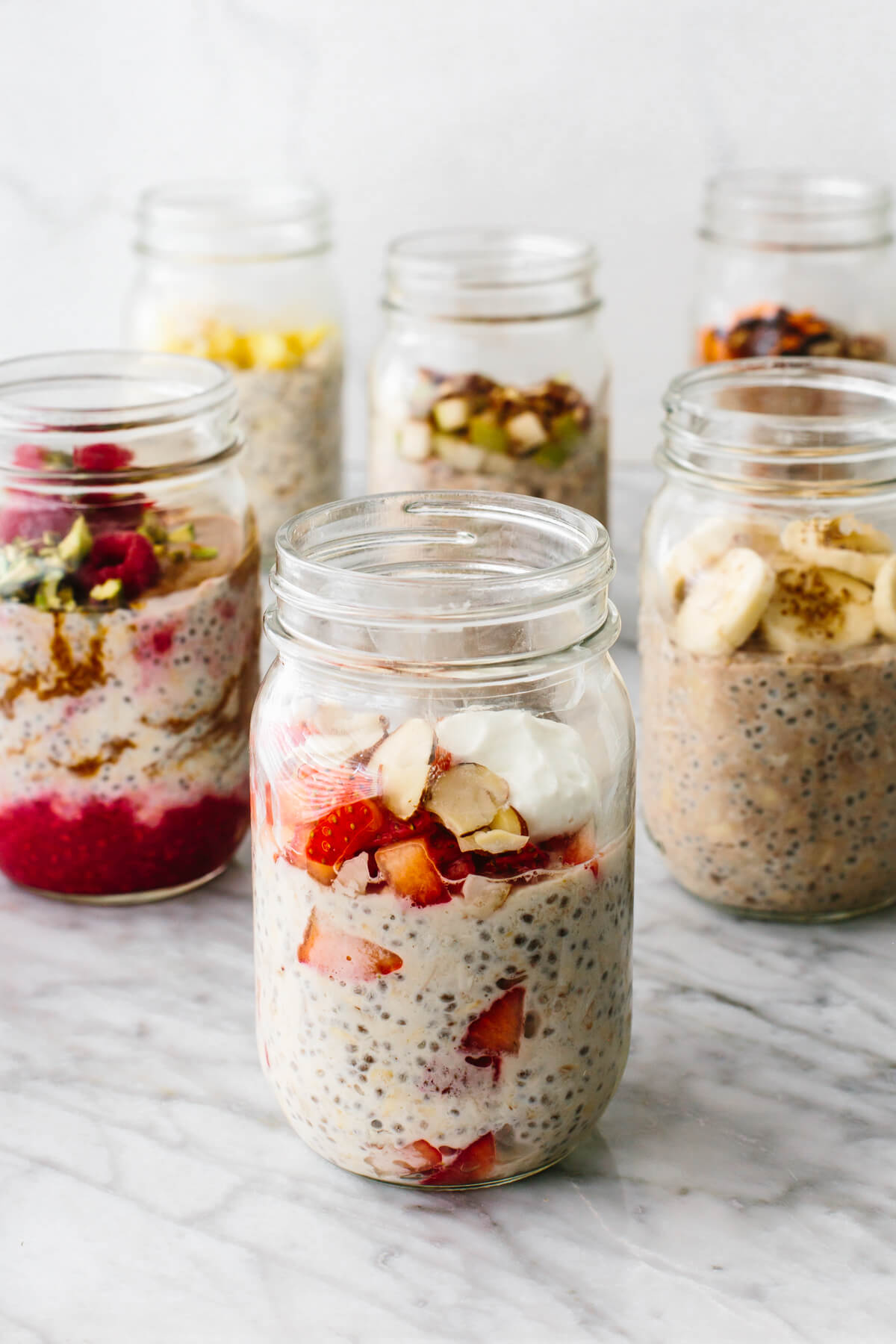 Overnight oats in a few jars with fruits on a table.