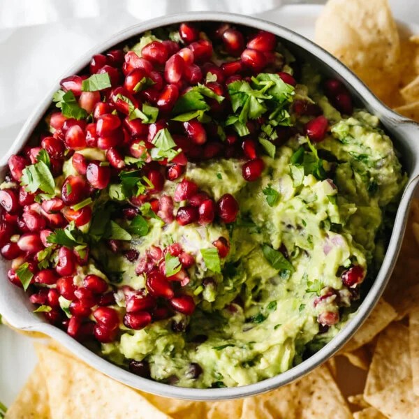 Pomegranate guacamole in a bowl surrounded by tortilla chips.