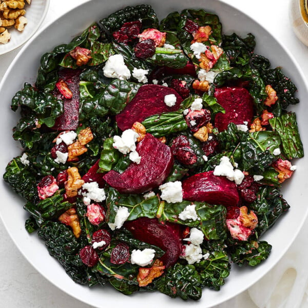 A large bowl of roasted beet salad next to toppings
