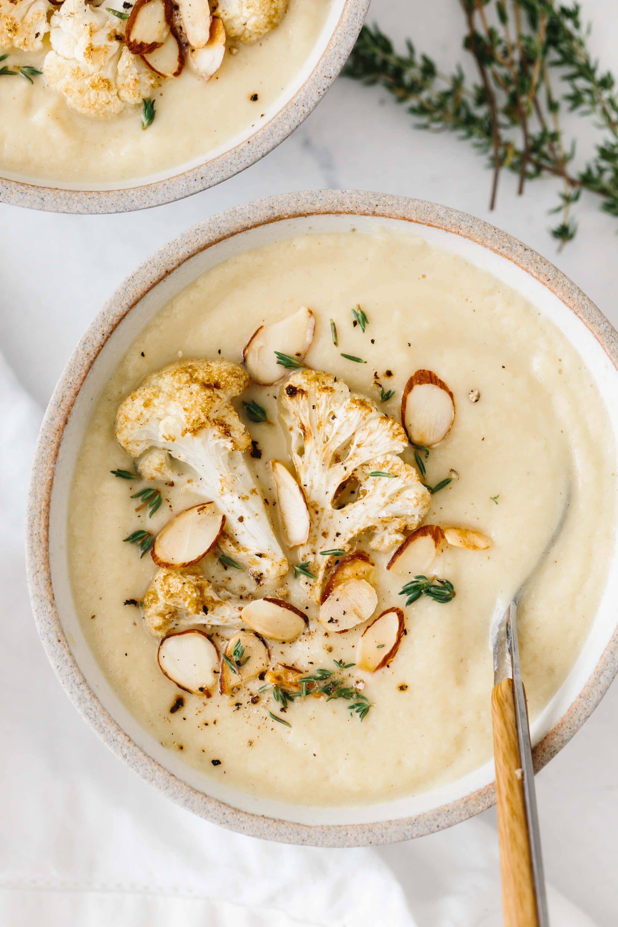 Roasted Cauliflower soup in a bowl, topped with cauliflower, almonds and thyme.