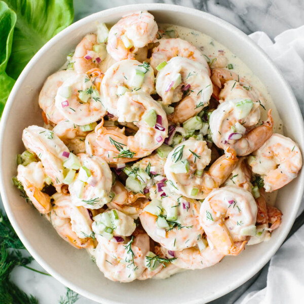 A white bowl with shrimp salad next to lettuces