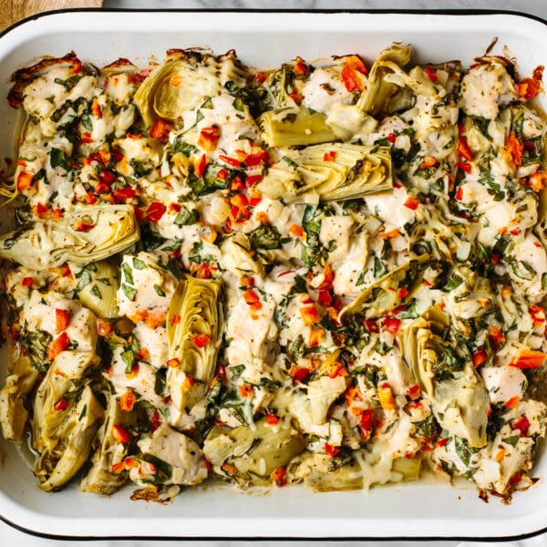 Spinach artichoke chicken bake in a pan next to wooden spoons