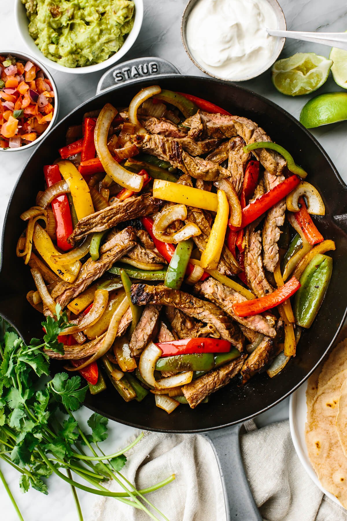 Steak fajitas in a skillet with toppings on the side