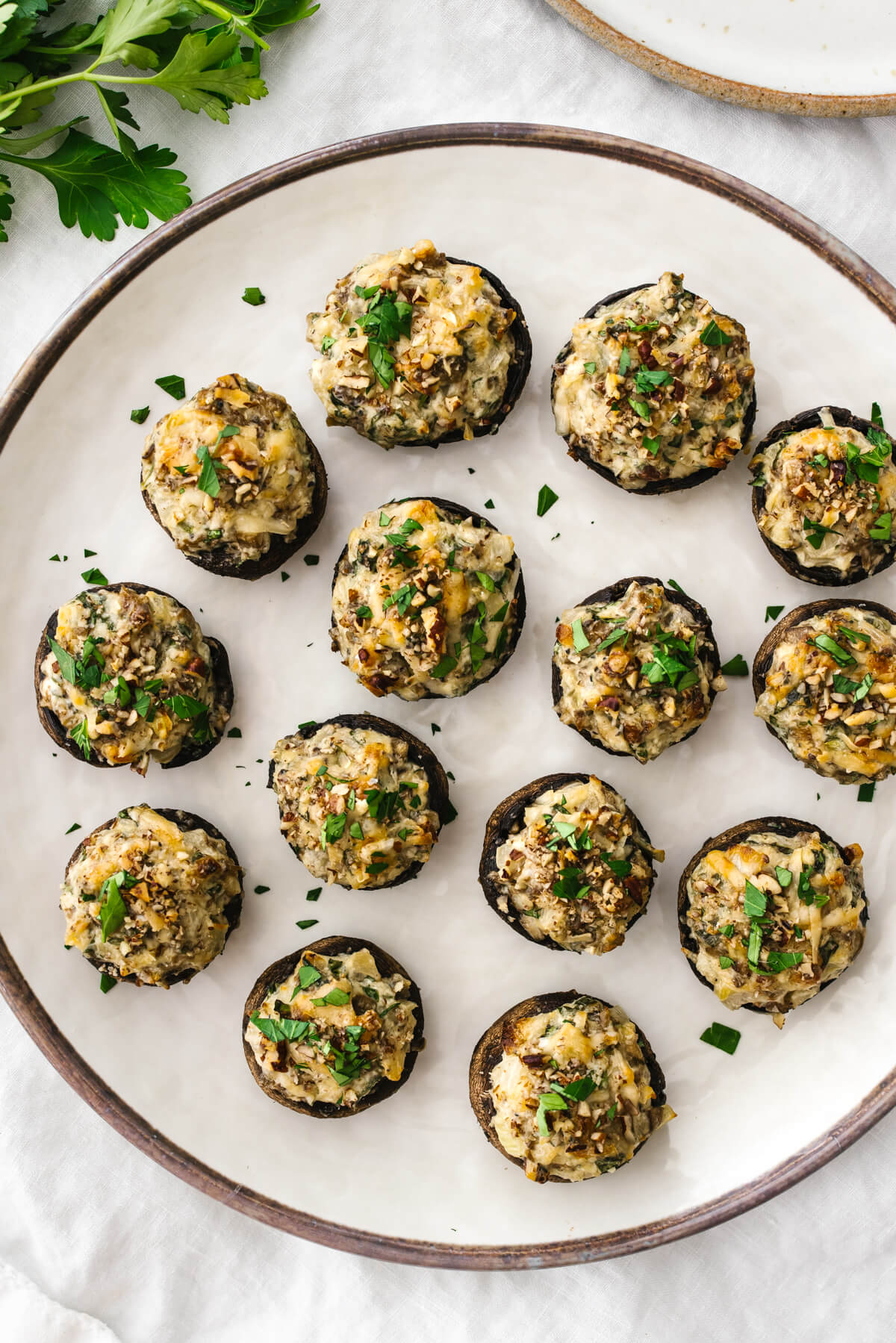 A white plate of stuffed mushrooms next to cilantro.