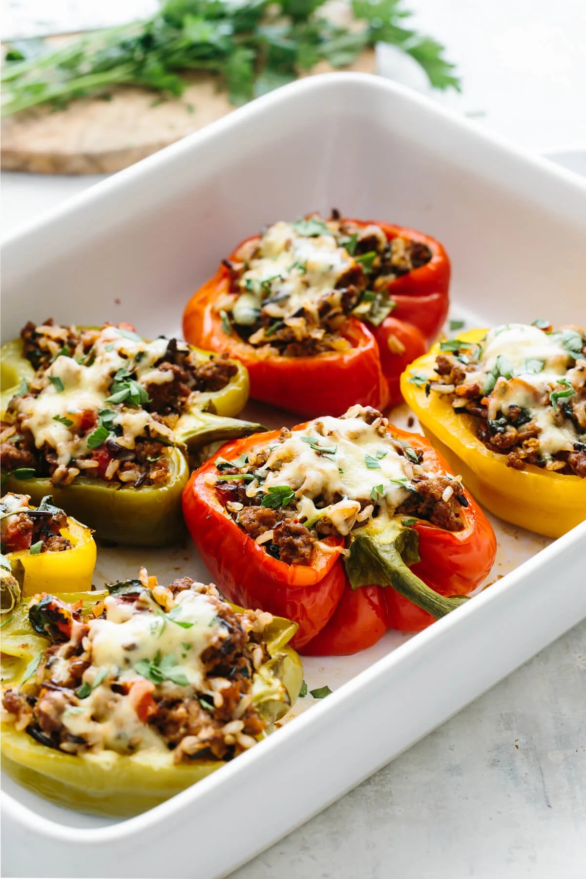 Different colored stuffed bell peppers in a white baking pan.