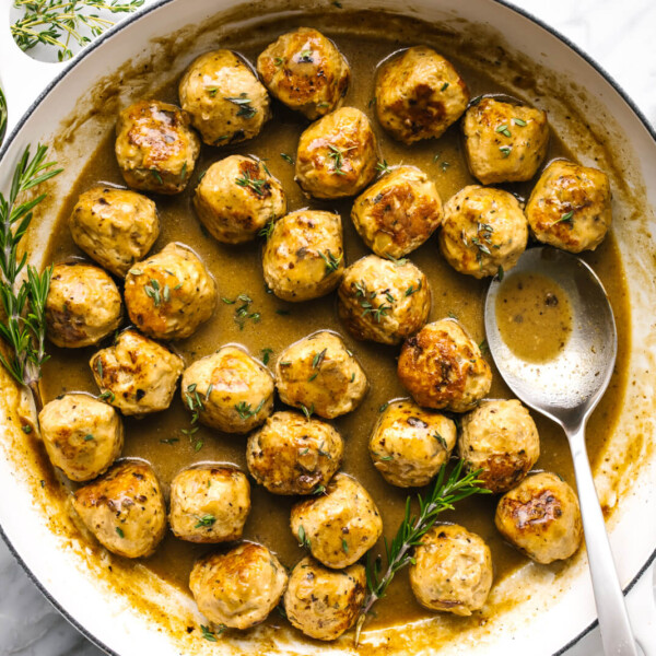 a large pan with turkey meatballs next to fresh herbs